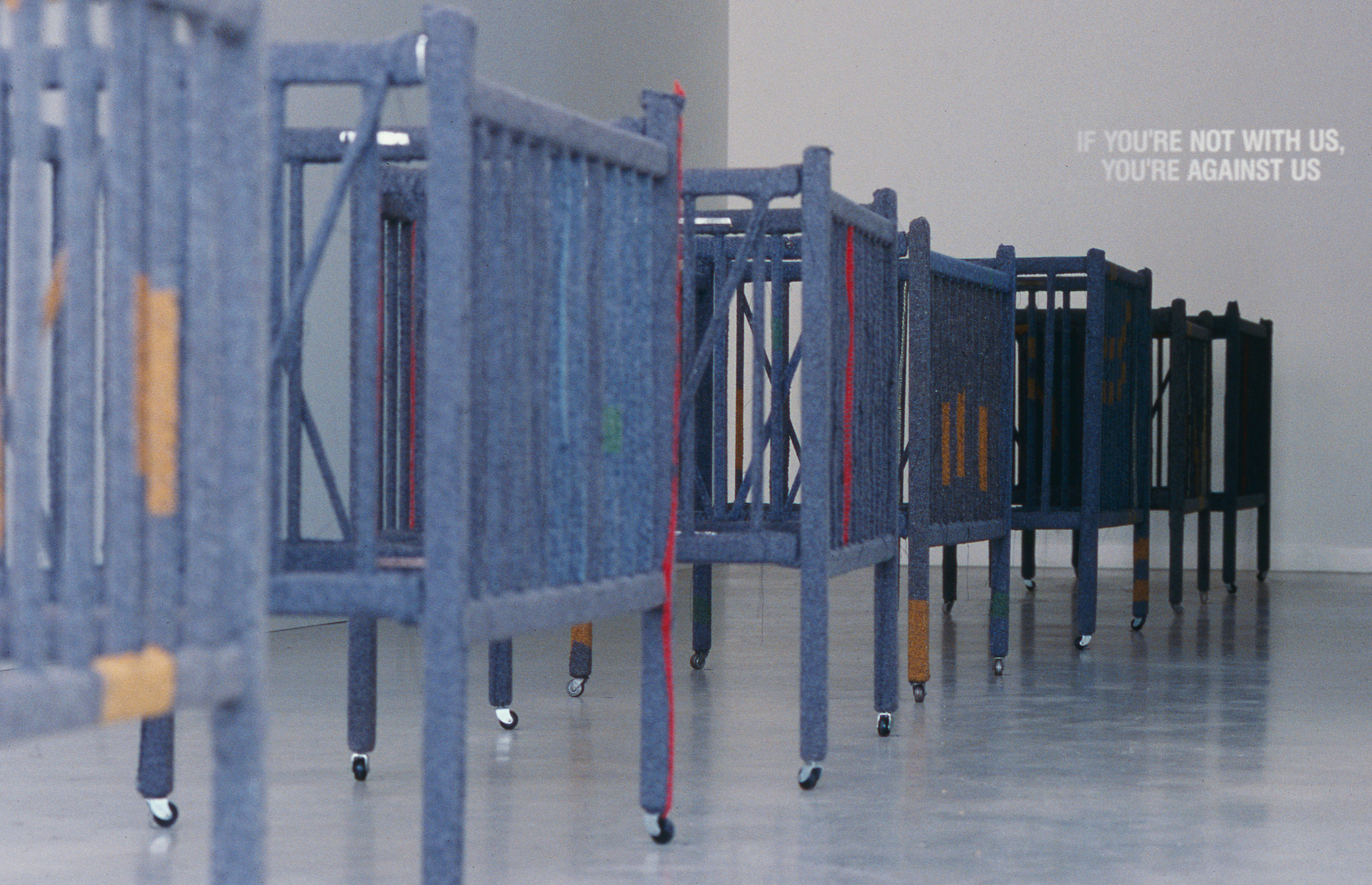 Olga Cironis, Under Cover, 2002, repurposed wooden cots, military blankets, cotton thread and castors with projected wall text, installation dimensions variable