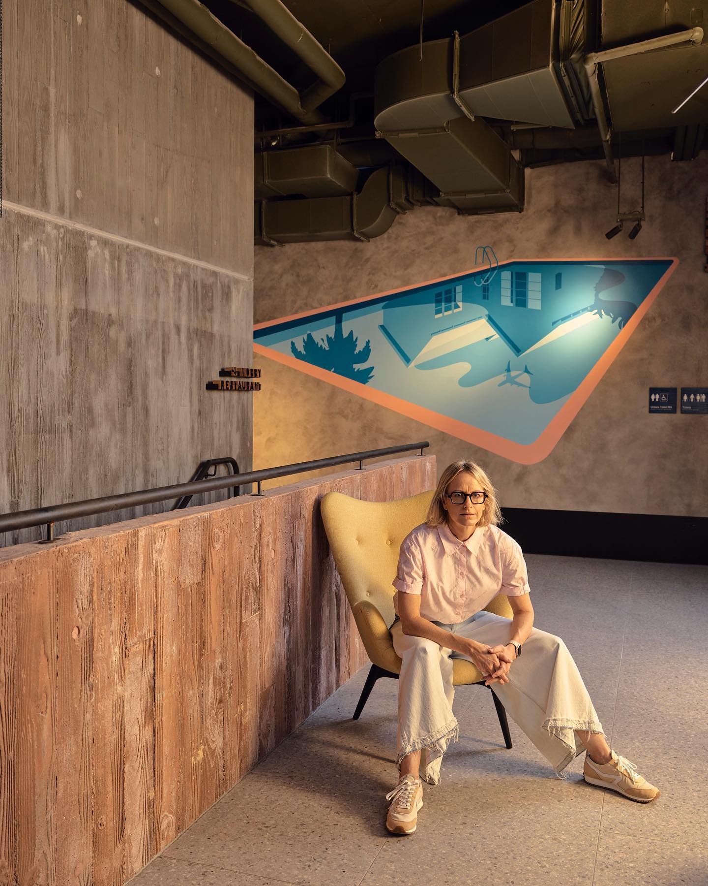 Joanna Lamb sits on a chair with painting of pool in background